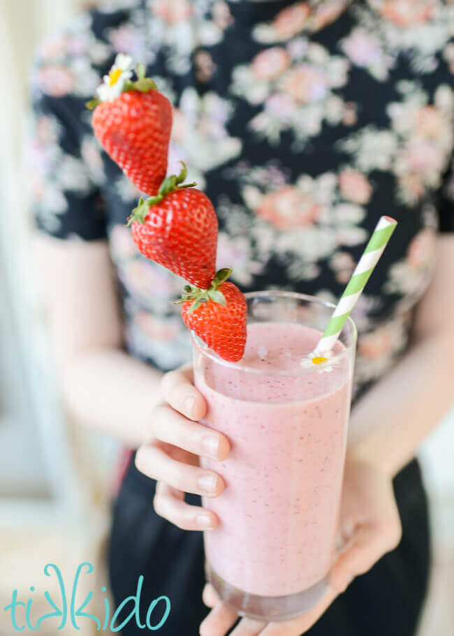 Strawberry milkshake being held by woman wearing a floral shirt.