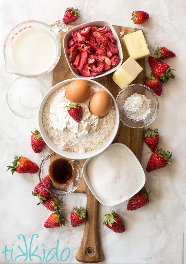 Strawberry muffin ingredients on a wooden cutting board on a white marble surface.