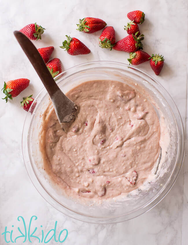 Strawberry muffin batter in a clear bowl on a white marble surface.