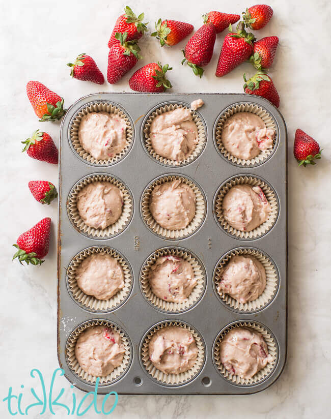 Strawberry muffin batter in a lined muffin tin, surrounded by fresh strawberries.