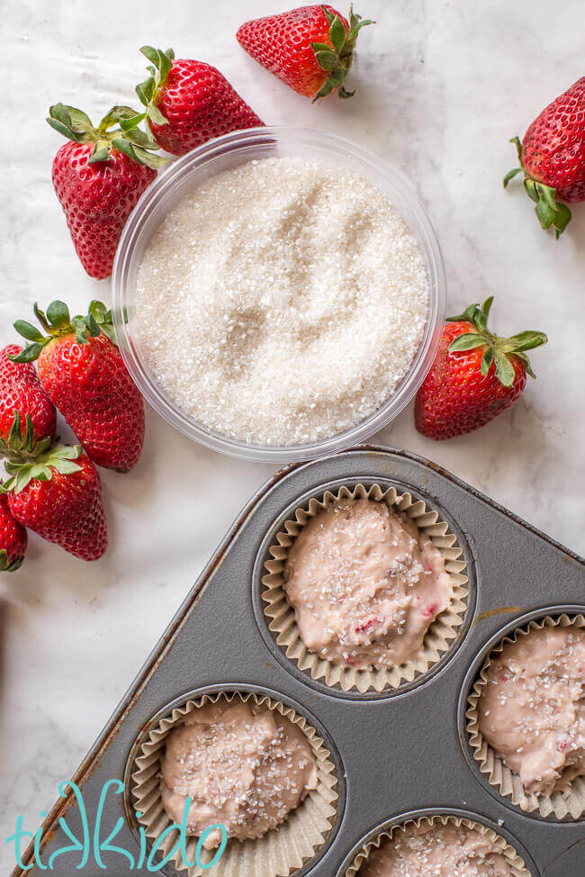 Coarse sugar being sprinkled on strawberry muffin batter.