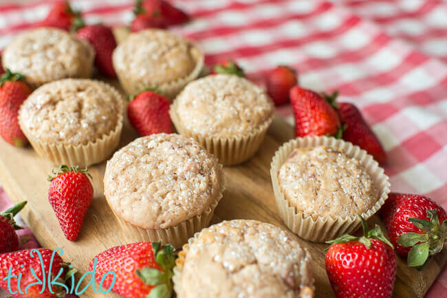 Strawberry muffins surrounded by fresh strawberries on a wooden cutting board.