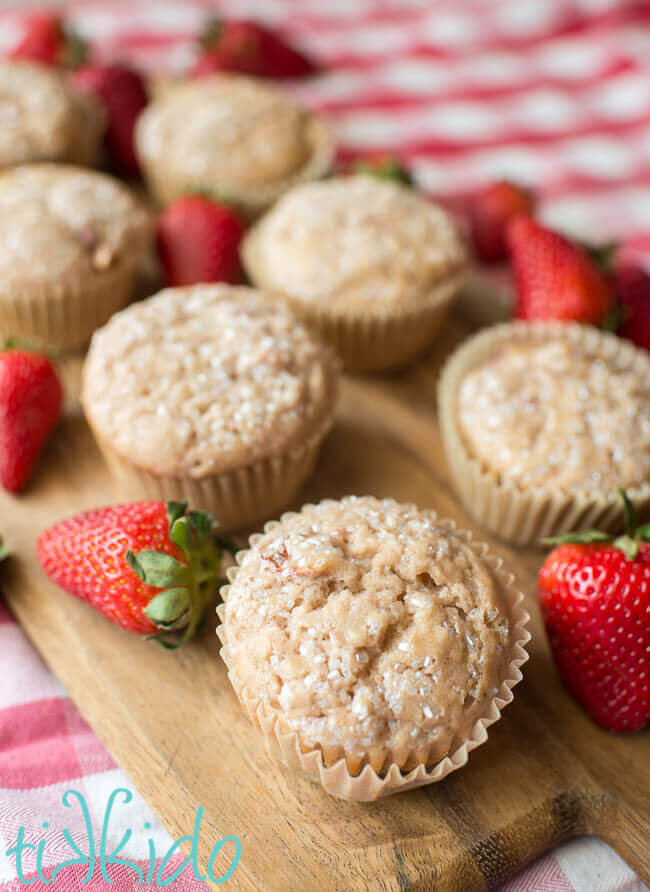 Strawberry muffins surrounded by fresh strawberries on a wooden cutting board.