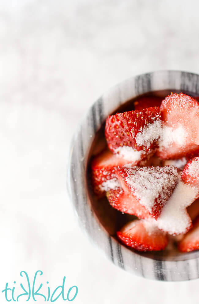 Marble bowl filled with sliced strawberries sprinkled with sugar.