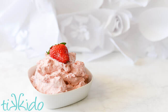 Bowl of strawberry whipped cream topped with a strawberry.