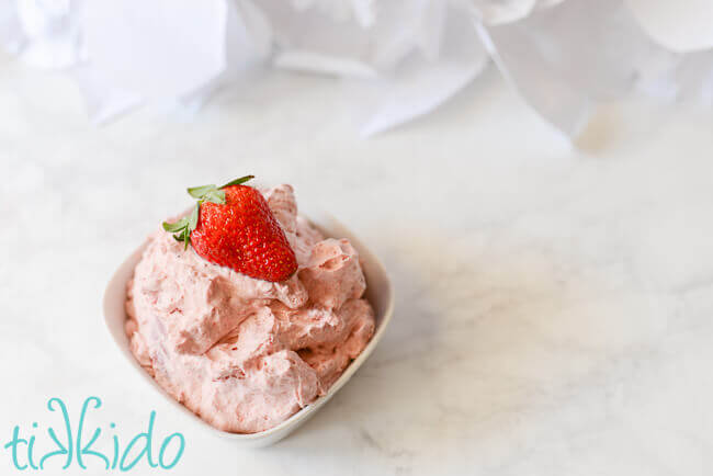 Bowl of strawberry whipped cream topped with a fresh strawberry.