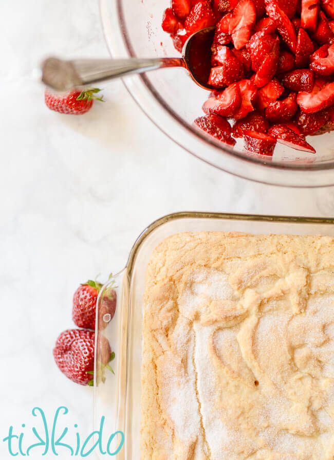 Pan of homemade strawberry shortcake and bowl of freshly sliced strawberries in a bowl.