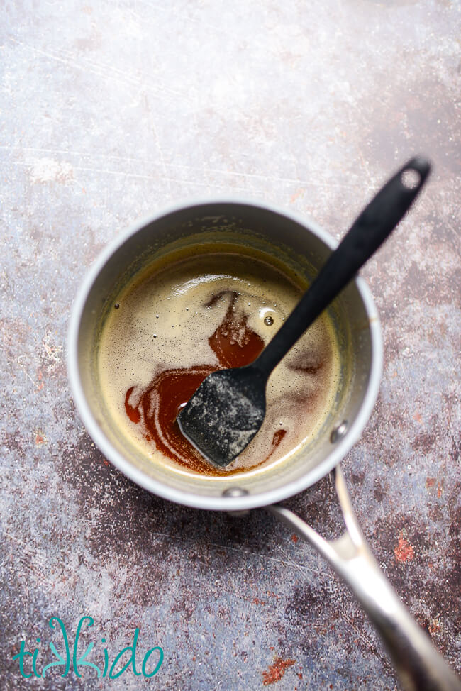 Browned butter in a small saucepan on a grey background.