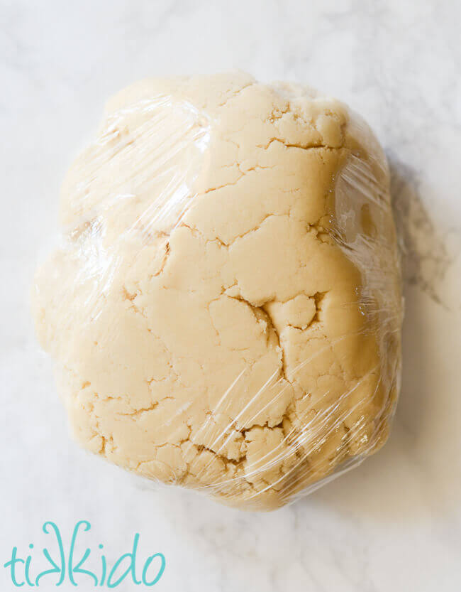 Sugar cookie dough wrapped in plastic wrap on a white marble surface.