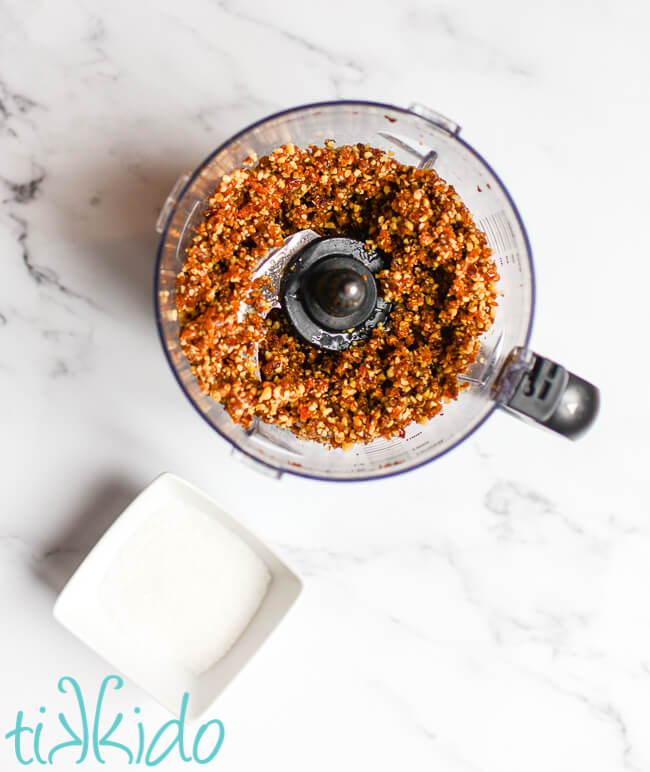 Ingredients for sugar plums mixed together in a food processor, on a white marble surface.