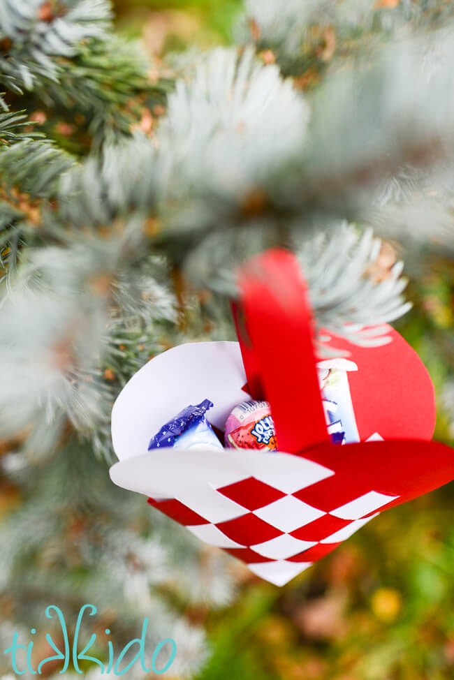 Swedish Paper Heart basket filled with candy and hanging from a Christmas tree.