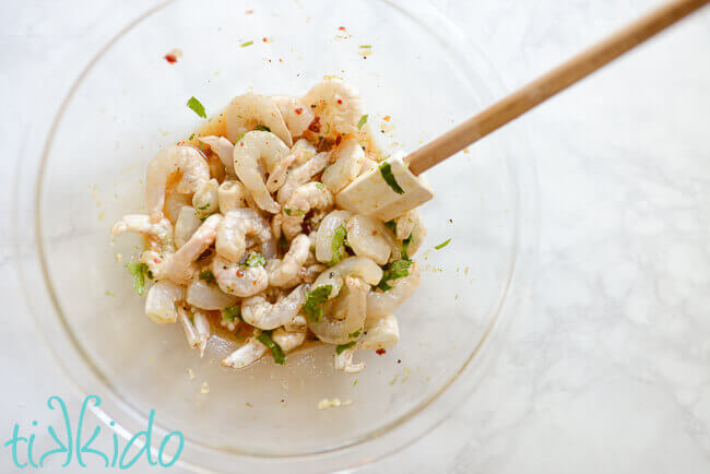 shrimp and tequila lime marinade in a clear glass bowl on a white marble surface.