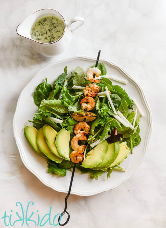 Salad topped with grilled tequila lime shrimp, avocado, and jicama, on a white plate.