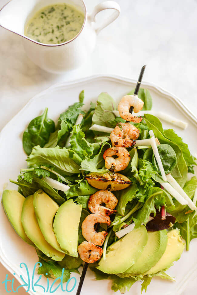 Salad topped with grilled tequila lime shrimp, avocado, and jicama, on a white plate.
