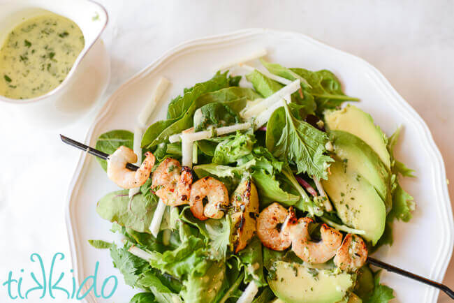 Salad topped with grilled tequila lime shrimp, avocado, and jicama, on a white plate.