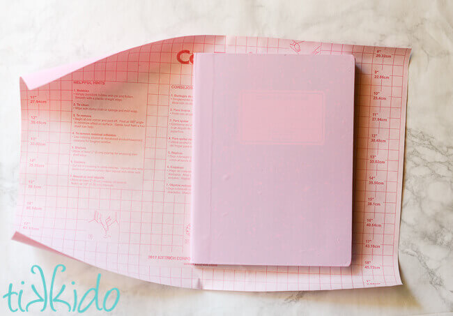 Composition notebook being covered in pink contact paper