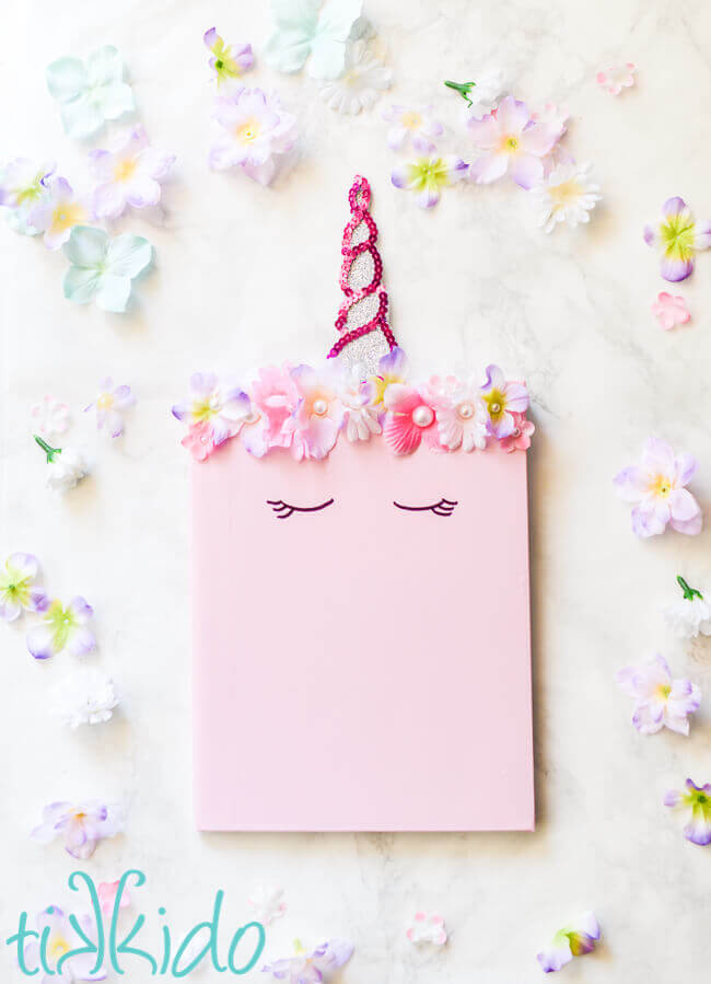DIY unicorn composition notebook with unicorn horn bookmark, surrounded by flowers.