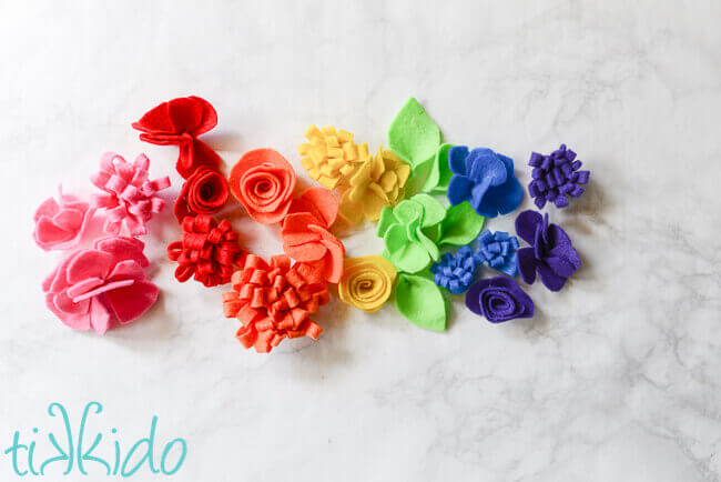 Rainbow of simple felt flowers on a white marble background.