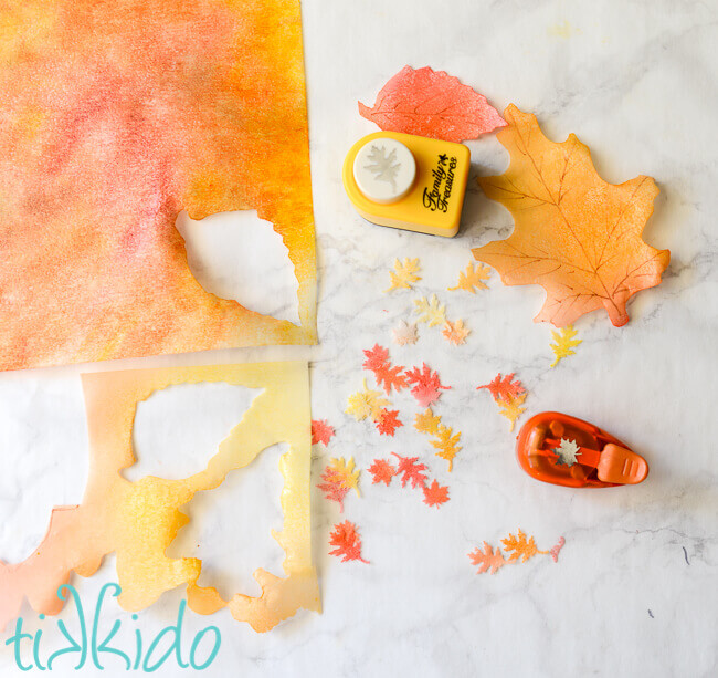 Colored edible wafer paper being cut into fall leaf shapes with punches.