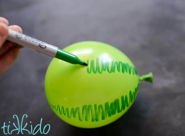 Lines being drawn on a green balloon with a green sharpie to make the balloon look like a watermelon.
