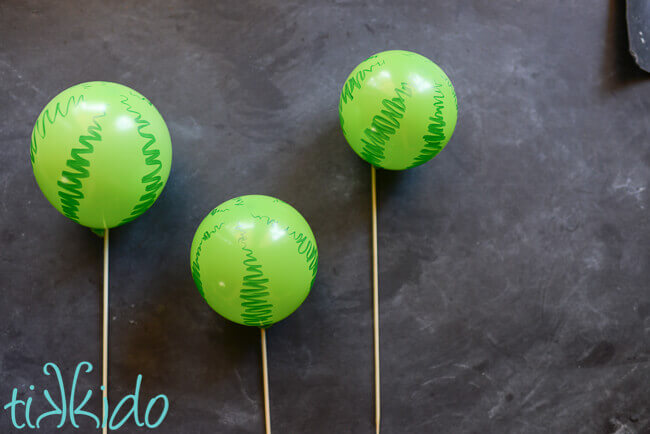 Three green balloons decorated to look like watermelons on a chalkboard background.