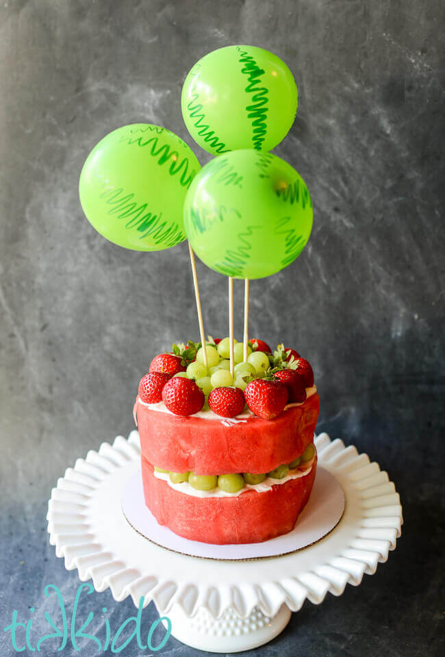 Watermelon and other fruit cut and arranged to look like a cake, with watermelon balloons cake topper.