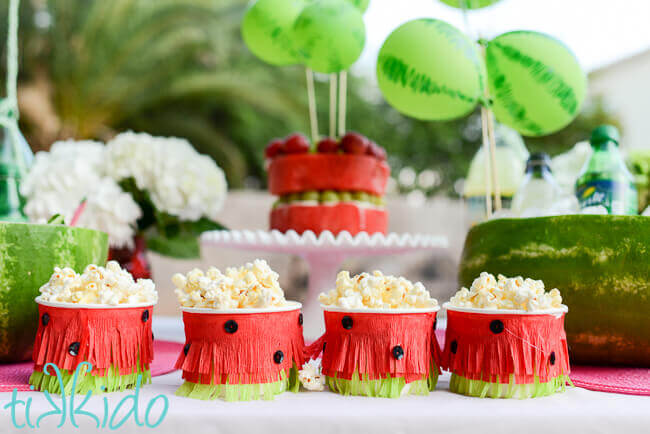 Snack cups decorated to fit a watermelon theme and filled with popcorn.