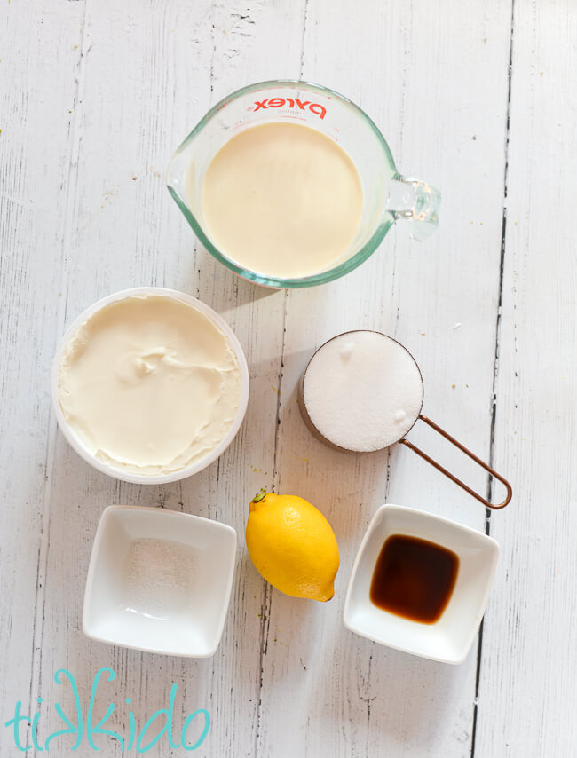 Ingredients for whipped mascarpone cake filling on a white wooden surface.