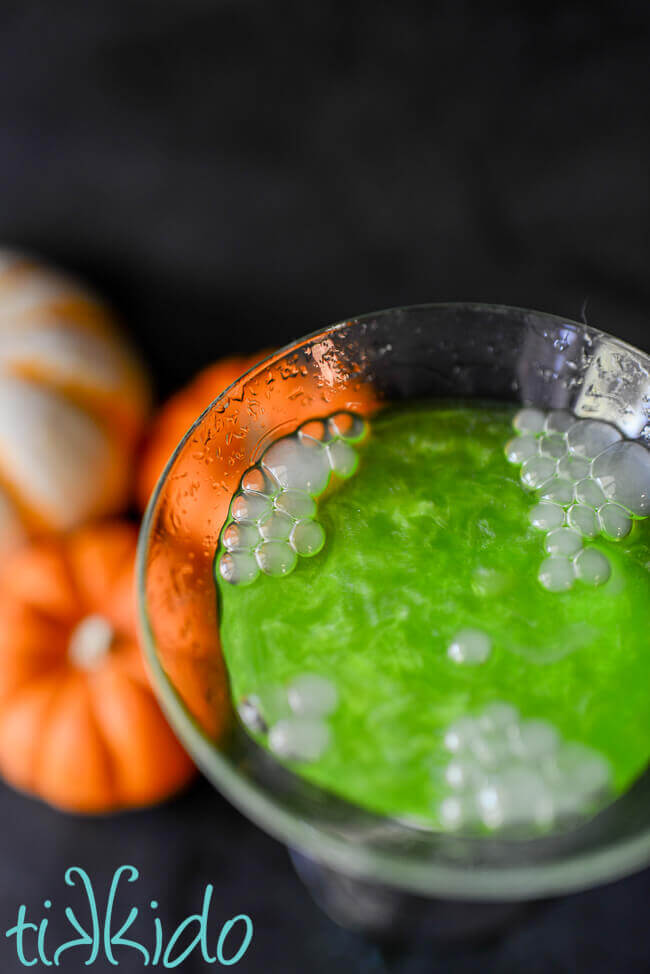 Closeup of a shimmering green Halloween cocktail with bubbles of dry ice smoke about to burst on the surface.