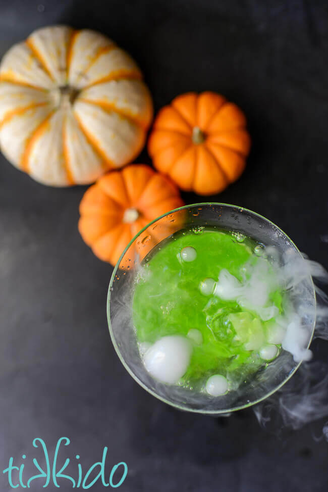 Overhead shot of a green, shimmery Halloween cocktail bubbling with dry ice smoke.