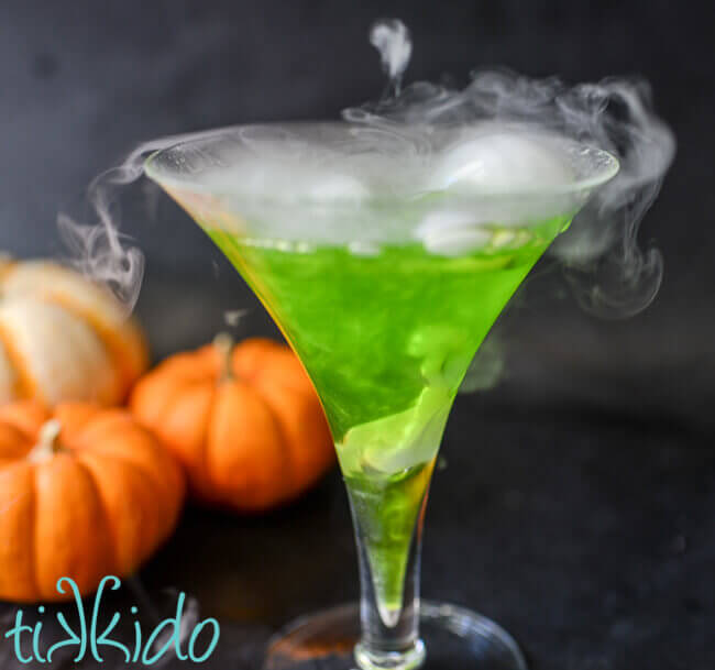 Side view of a shimmery green Halloween cocktail bubbling and smoking with dry ice.