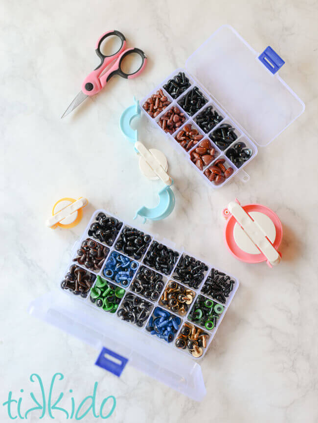 Pom pom makers, scissors, and stuffed animal eyes and noses on a white marble background.
