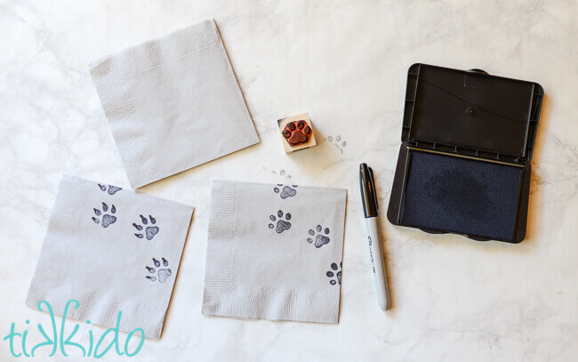 Paper napkins being stamped with paw prints to make wolf napkins for a wolf birthday party