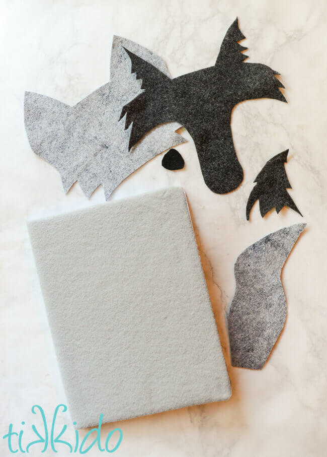 Composition notebook covered in a layer of felt, next to felt cut in shapes of a wolf face and tail.