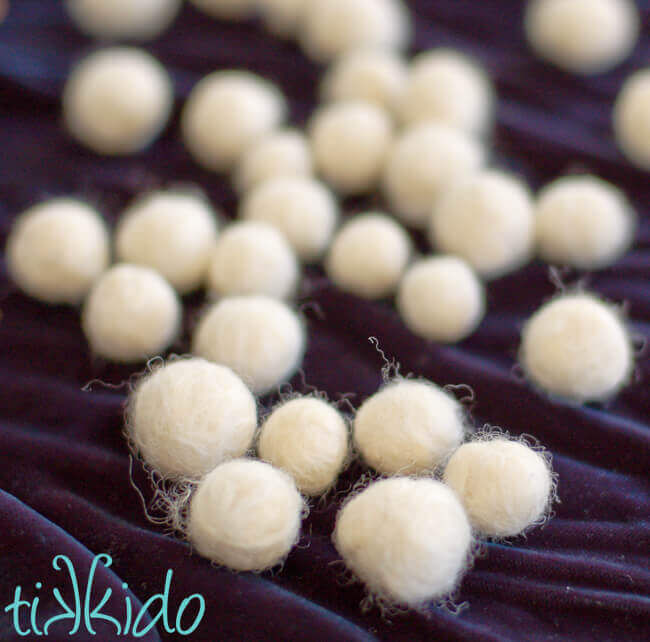 Scattered white wool felt balls on a dark blue velvet background.
