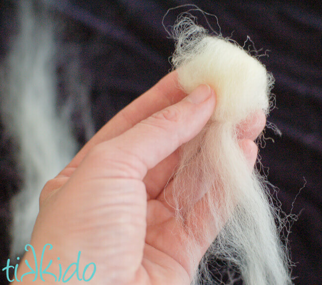 Hand holding wool roving being wound into a ball.