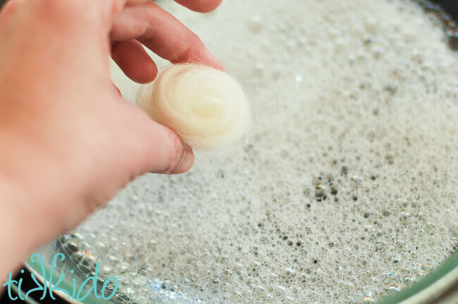 Hand holding wound wool roving over soapy water before felting using a wet felting method.