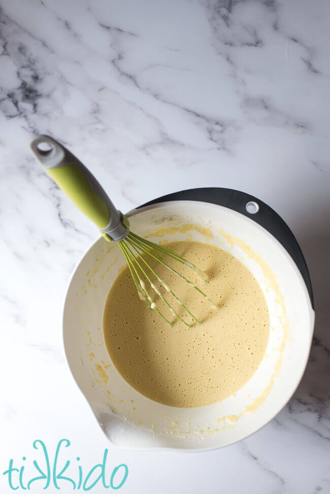 Yorkshire pudding batter in a bowl with a whisk on a white marble background.