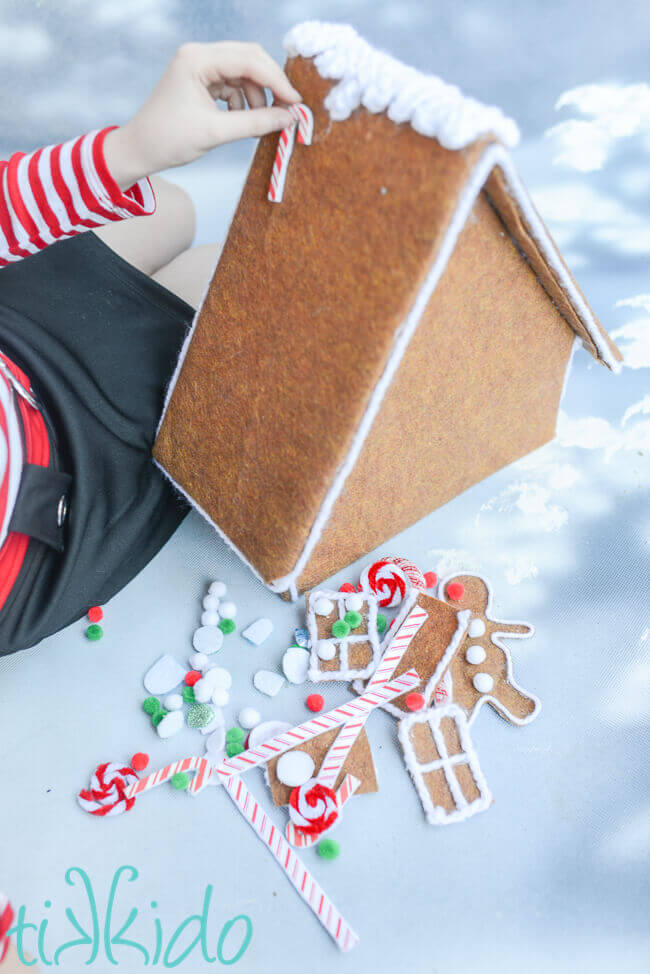 Little girl's hand putting a fake candy cane on a felt gingerbread house.