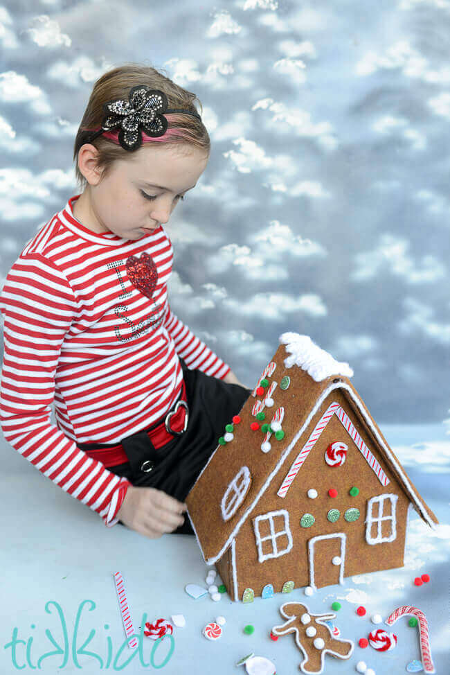 Little girl decorating a felt gingerbread house toy with felt fake candy decorations.