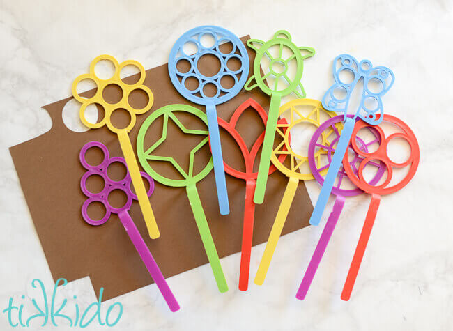 Colorful bubble wands and brown scrapbook paper on a white marble background.