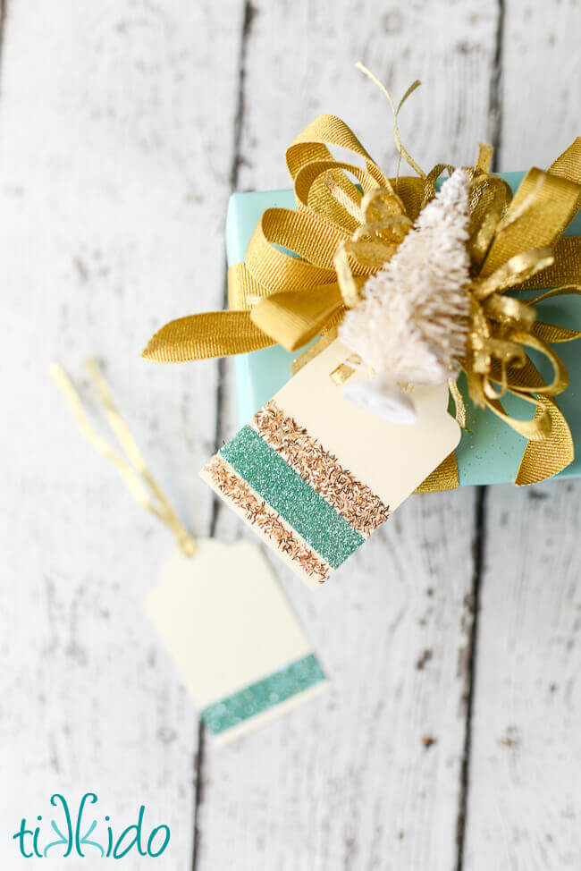 Christmas present wrapped in aqua and gold, topped with a bottle brush tree and a DIY Gift Tag