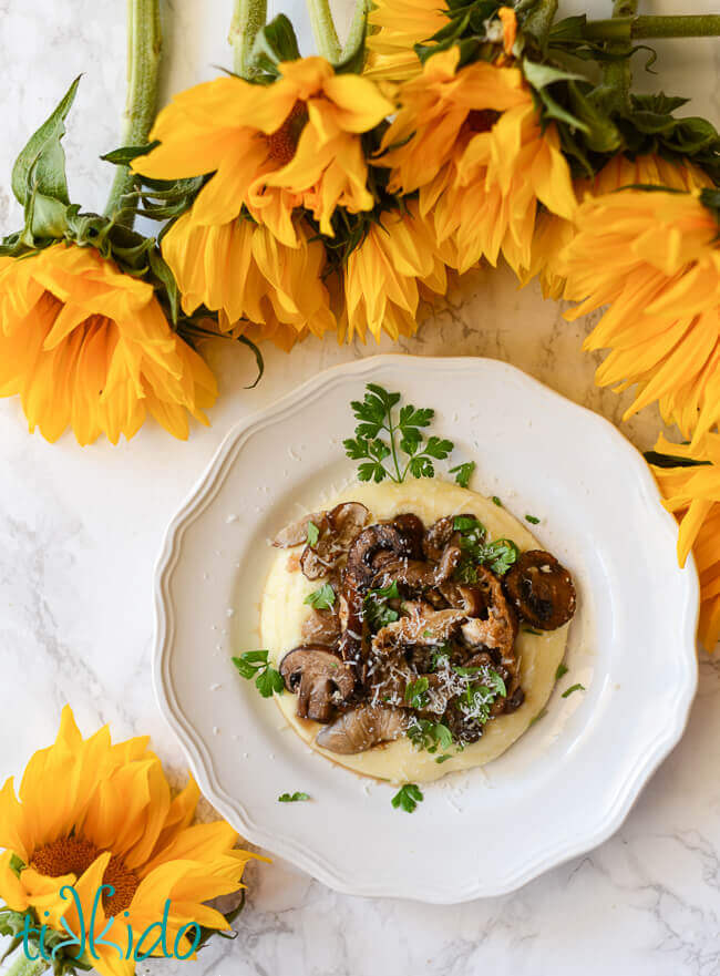 Easy polenta and oven roasted mushrooms on a white plate, surrounded by sunflowers.