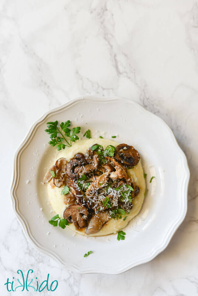 Oven roasted mushrooms topping oven baked polenta on a white plate.