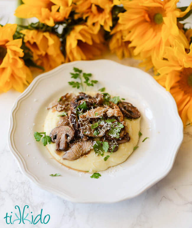 Cheesy polenta recipe topped with oven roasted mushrooms on a white plate.