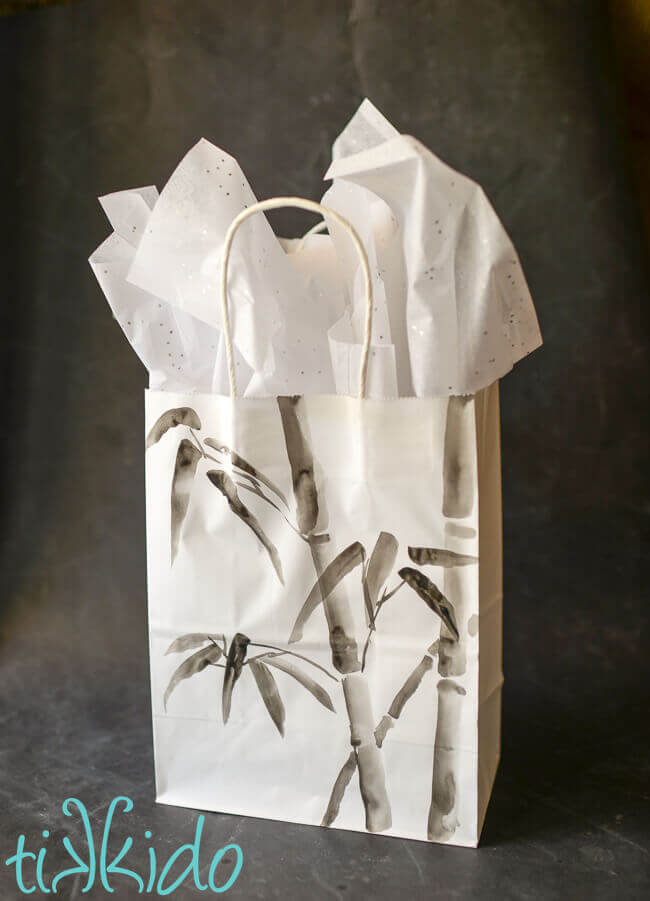 White gift bag painted with bamboo designs done in Japanese ink painting style, filled with tissue paper