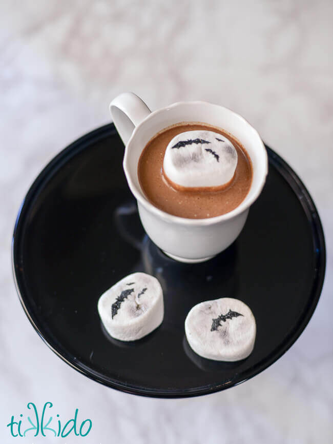 white cup full of hot chocolate, with a marshmallow that looks like a full moon floating in it.  Two more marshmallows beside the cup.