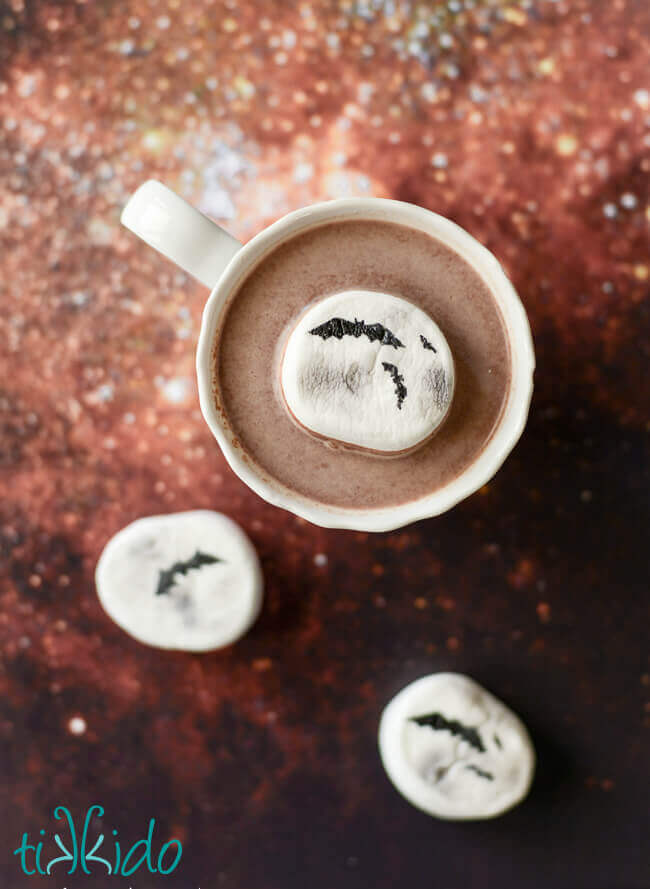 Cup of Halloween hot cocoa with a marshmallow decorated like a full moon with bat silhouettes.