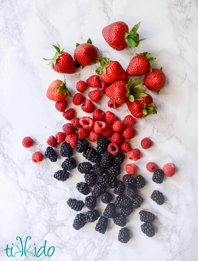 Strawberries, raspberries, and blackberries on a white marble surface.