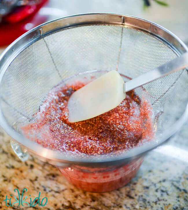 Raspberry simple syrup being strained of solids with a mesh strainer.